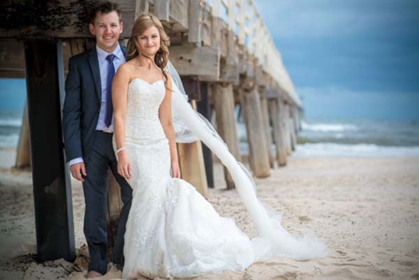 bride and groom on the beach under a pier